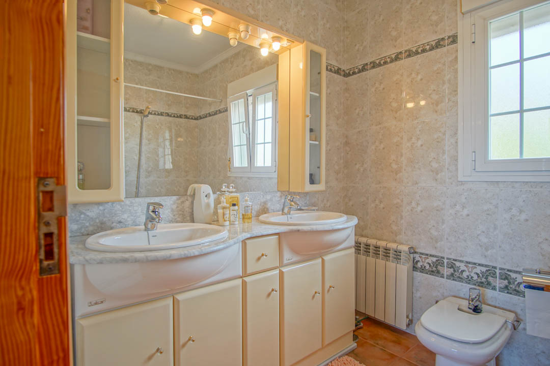 Bathroom with double vanity on marble countertop, solid wood cabinetry, integrated mirror lighting, and tiled walls with a classic decorative border.