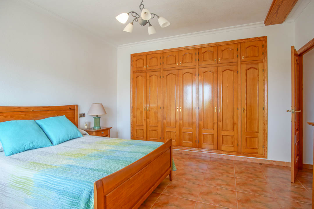 Bedroom featuring a large custom-made solid wood built-in wardrobe, matching wooden bed frame, and classic ceramic tile flooring.