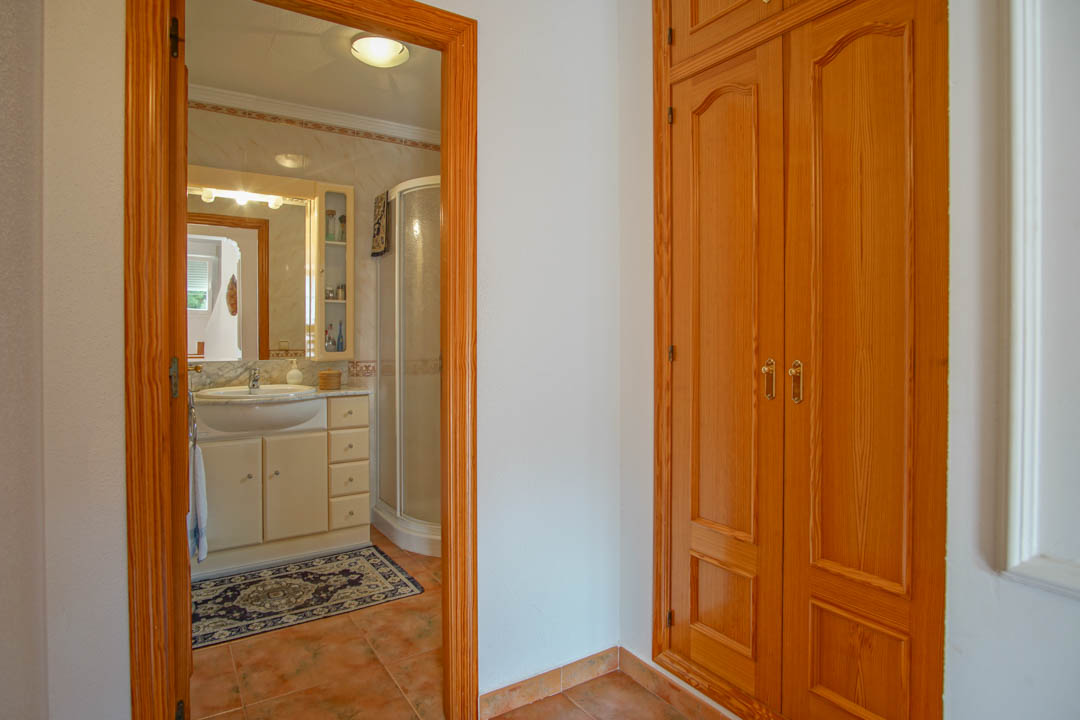 Bedroom featuring a solid wood built-in wardrobe and an ensuite bathroom equipped with a corner shower, marble vanity, and classic tiling.