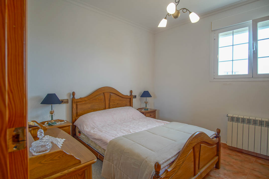 Bedroom featuring solid wood furniture, ceramic tile flooring, and a radiator. The space includes a matching bed frame and nightstands under light from a gridded window.