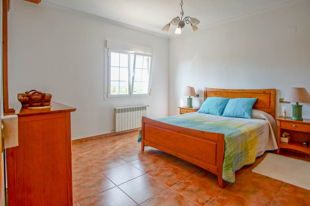 Bedroom featuring solid wood furniture, terracotta-style floor tiles, and a white-framed window equipped with a radiator for climate control.
