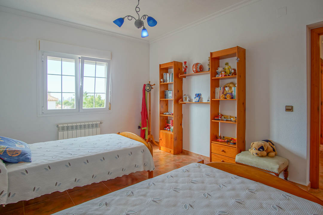 Bedroom featuring twin beds, solid wood shelving units, and ceramic tile flooring. It includes a wall-mounted radiator and a double-glazed window for natural light.