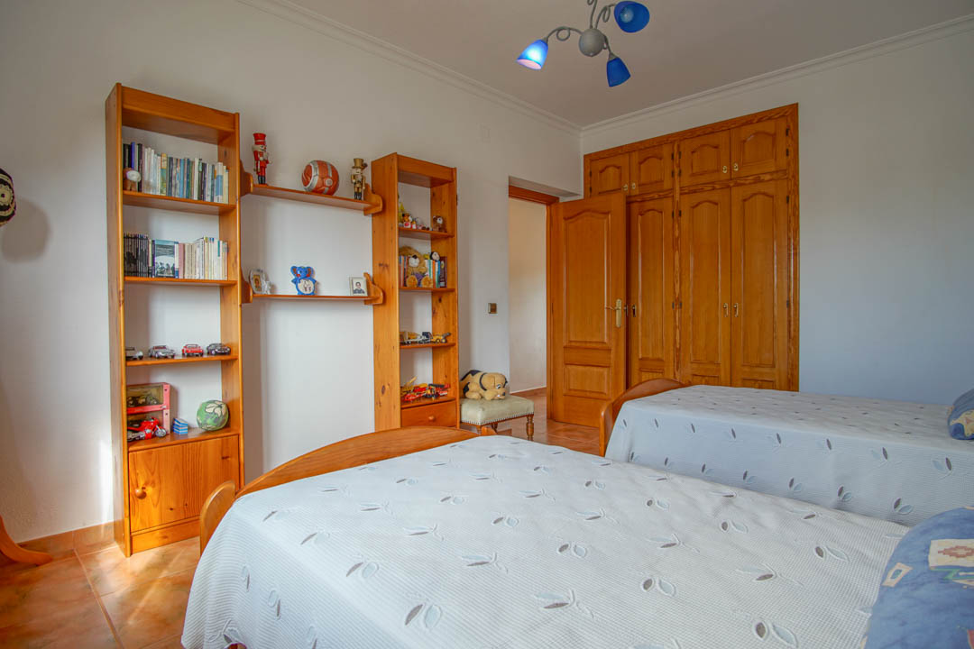 Bedroom featuring twin beds, solid wood shelving units, and custom-built wardrobes with traditional arched panels and tiled flooring.