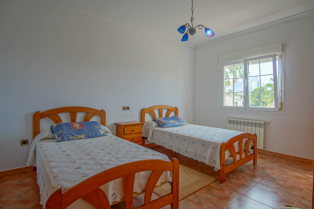 Bright bedroom featuring twin solid wood beds, ceramic tile flooring, and a window offering views of the surrounding palm trees and mountains.