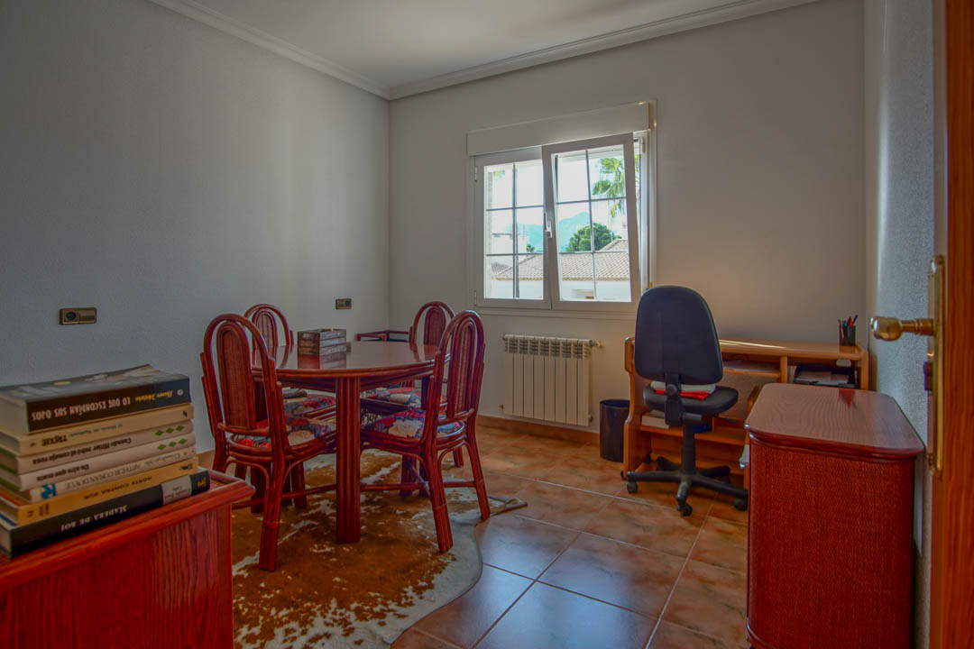 Bright home office featuring solid wood furniture, terracotta tile flooring, and a dedicated desk area. Large windows provide natural light and views of the surroundings.