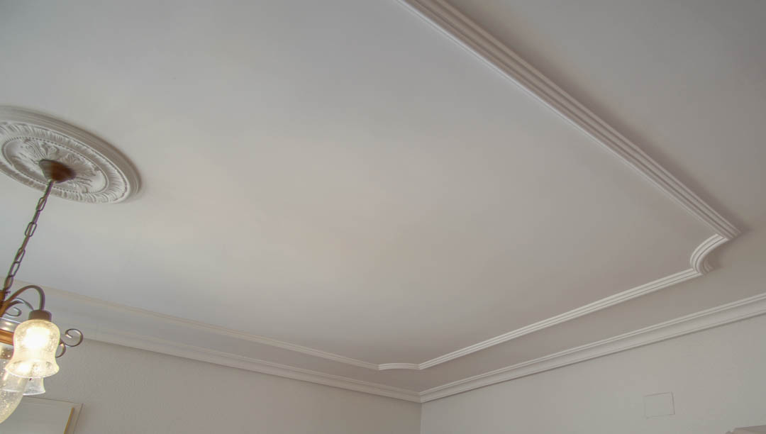 Detail of the ceiling featuring classic decorative moldings and a central plaster rose. The lighting includes a traditional chandelier with frosted glass shades.