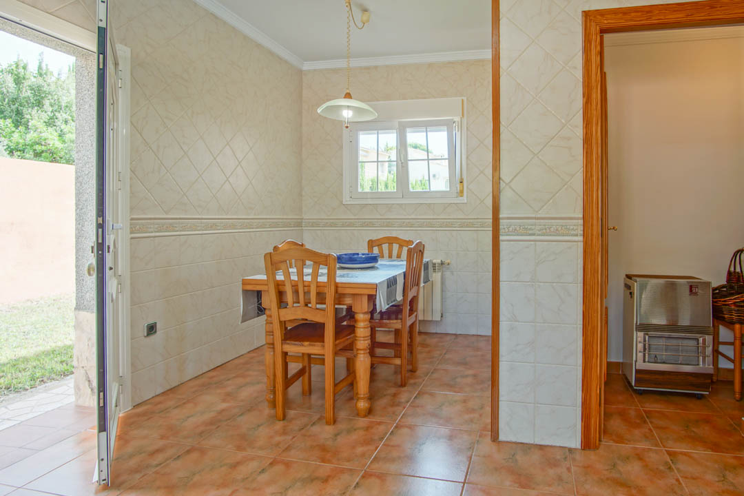 Dining area featuring solid wood furniture, decorative wall tiling, and direct access to the garden through a wide doorway.