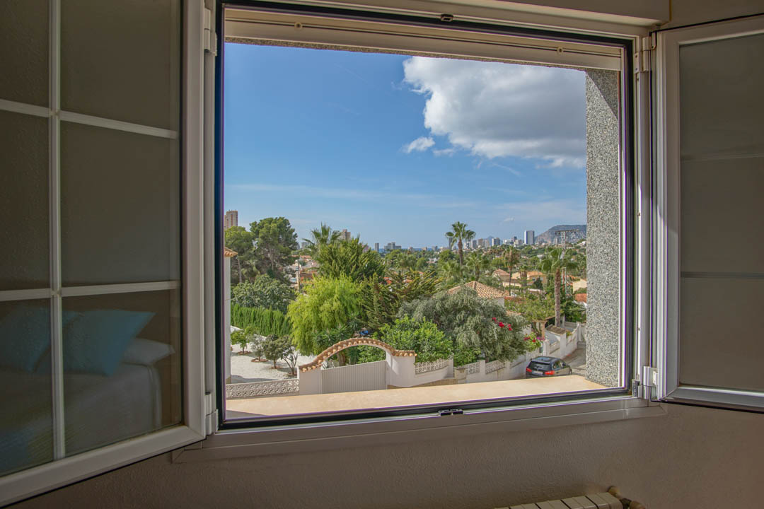Elevated view from the bedroom window overlooking the residential neighborhood, Mediterranean greenery, and the distant city skyline.