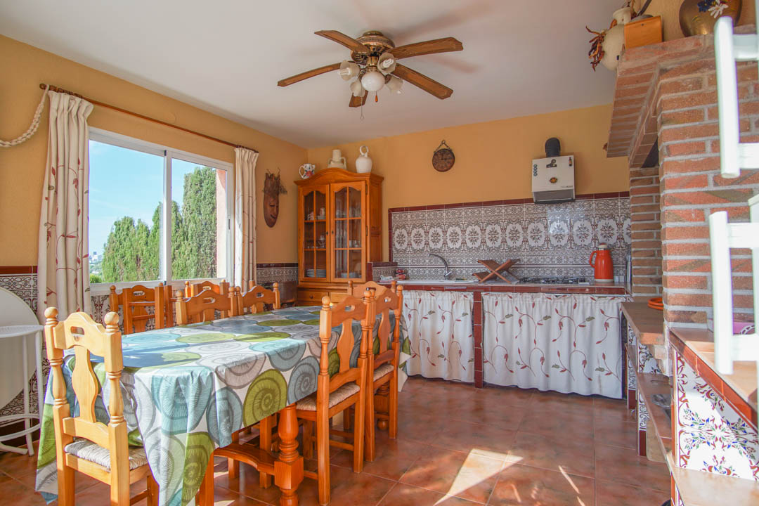 Enclosed outdoor kitchen and dining area featuring traditional patterned tiles, solid wood furniture, and a rustic brick fireplace structure.
