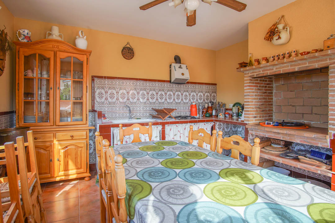 Enclosed outdoor kitchen featuring a built-in brick barbecue, solid wood cabinetry, and traditional patterned tile backsplashes with a rustic dining area.