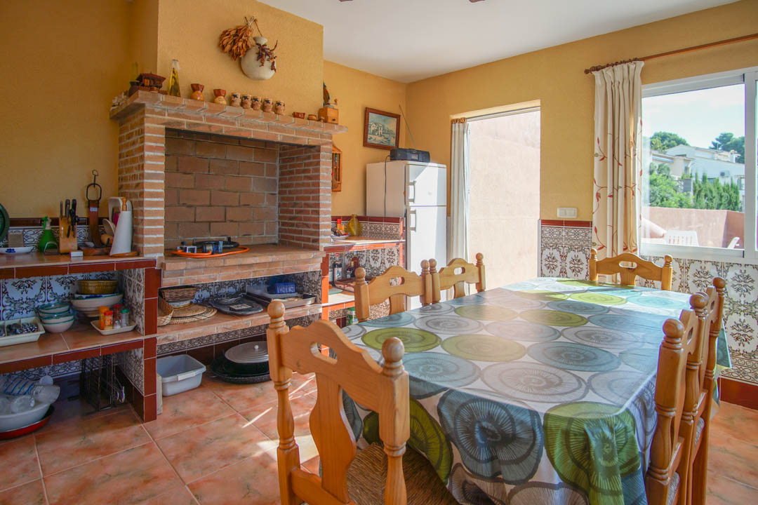 Enclosed outdoor kitchen featuring a large brick wood-fired oven, decorative tiled countertops, and a rustic wooden dining set on traditional terracotta flooring.