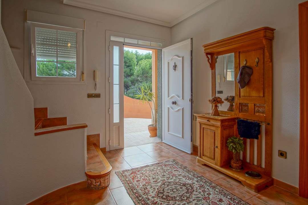 Entrance hall featuring a white paneled door, rustic ceramic tile flooring, and a solid wood hall stand with a mirror. Natural light illuminates the space from the open doorway.