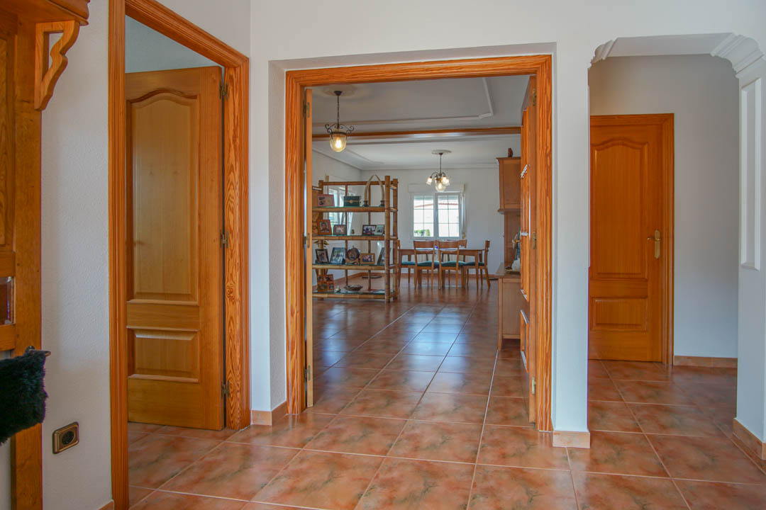 Entrance hall featuring ceramic tile flooring and solid wood door frames leading to a bright living and dining area with traditional wooden furnishings.
