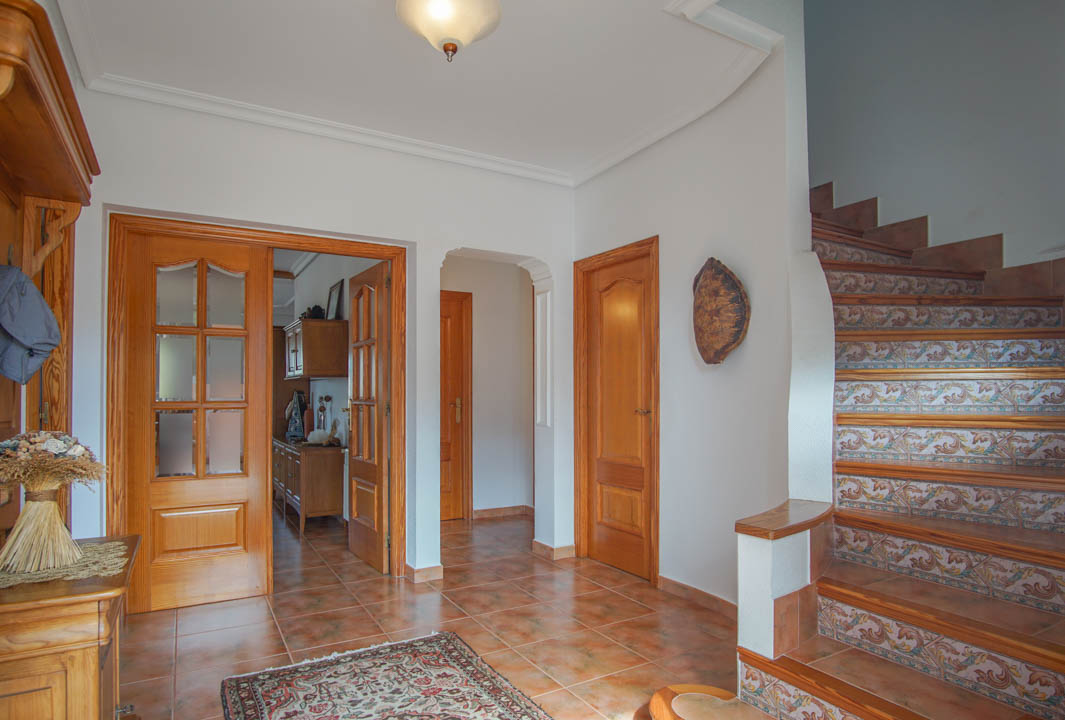 Entrance hall featuring terracotta-style floor tiles, solid wood doors, and a staircase with ornate ceramic tile risers and wooden treads.