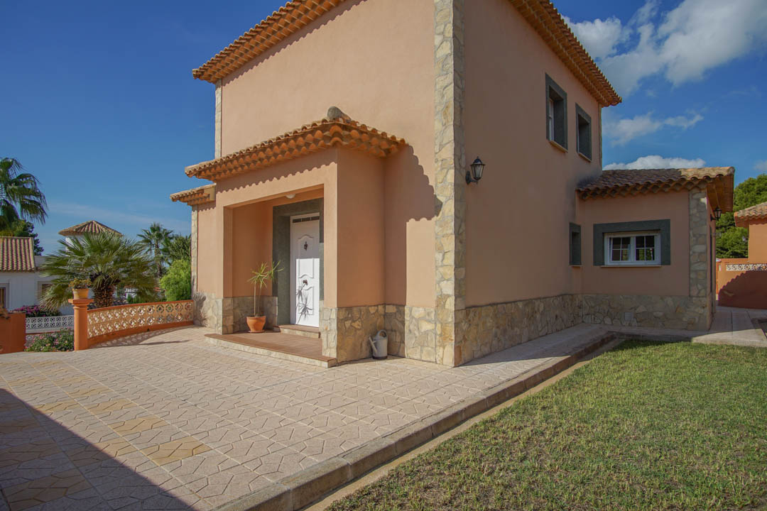 Exterior view featuring natural stone cladding, a recessed main entrance porch, and patterned stone paving adjacent to a manicured lawn.
