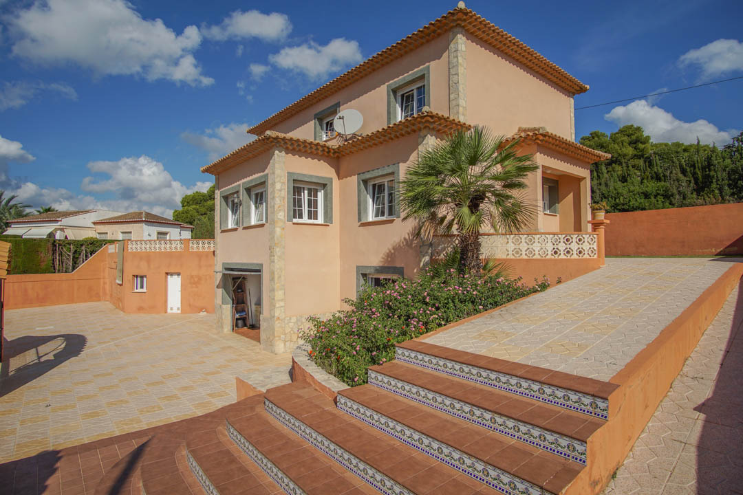 Exterior view of the three-story villa featuring earth-toned facades, traditional tiled steps with ceramic accents, and a spacious paved driveway.