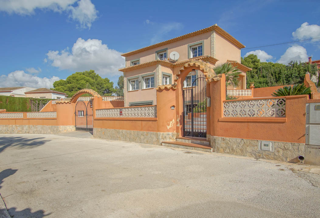 Exterior view of the three-story villa featuring terracotta walls, natural stone base, and arched wrought iron gates for pedestrian and vehicle access.