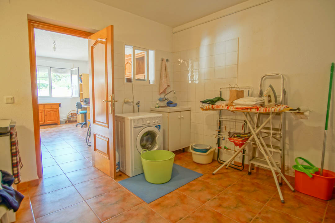 Functional laundry room featuring a washing machine, utility sink, and tiled walls, connected via a solid wood door to an adjacent bright room.