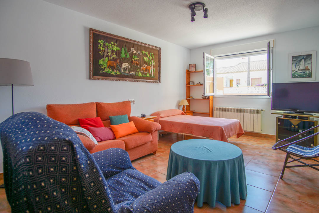 Functional living space with ceramic tile flooring, featuring a seating area, single bed, and a large window that fills the room with natural light.