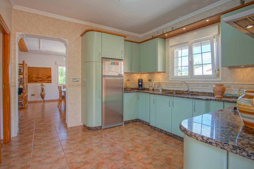 Independent kitchen featuring mint green cabinetry, granite countertops, and ceramic flooring. An arched doorway leads to the dining area, showcasing a practical layout.