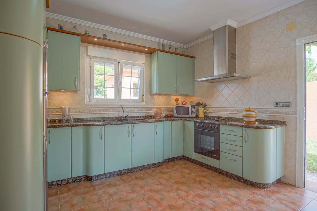 Independent kitchen featuring mint green cabinetry with curved edges, granite countertops, and integrated appliances. Tiled walls and recessed lighting complete the space.