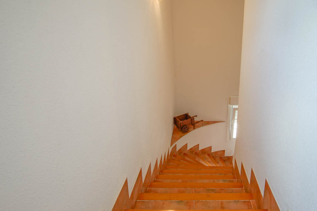 Internal staircase featuring terracotta-style tiling and wood-trimmed steps, set between textured white walls with a natural light source.