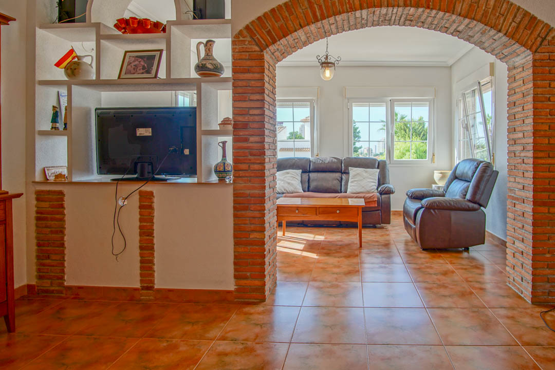 Living area featuring a prominent exposed brick archway, terracotta-style tiling, and a built-in media unit leading to a bright lounge with leather seating.