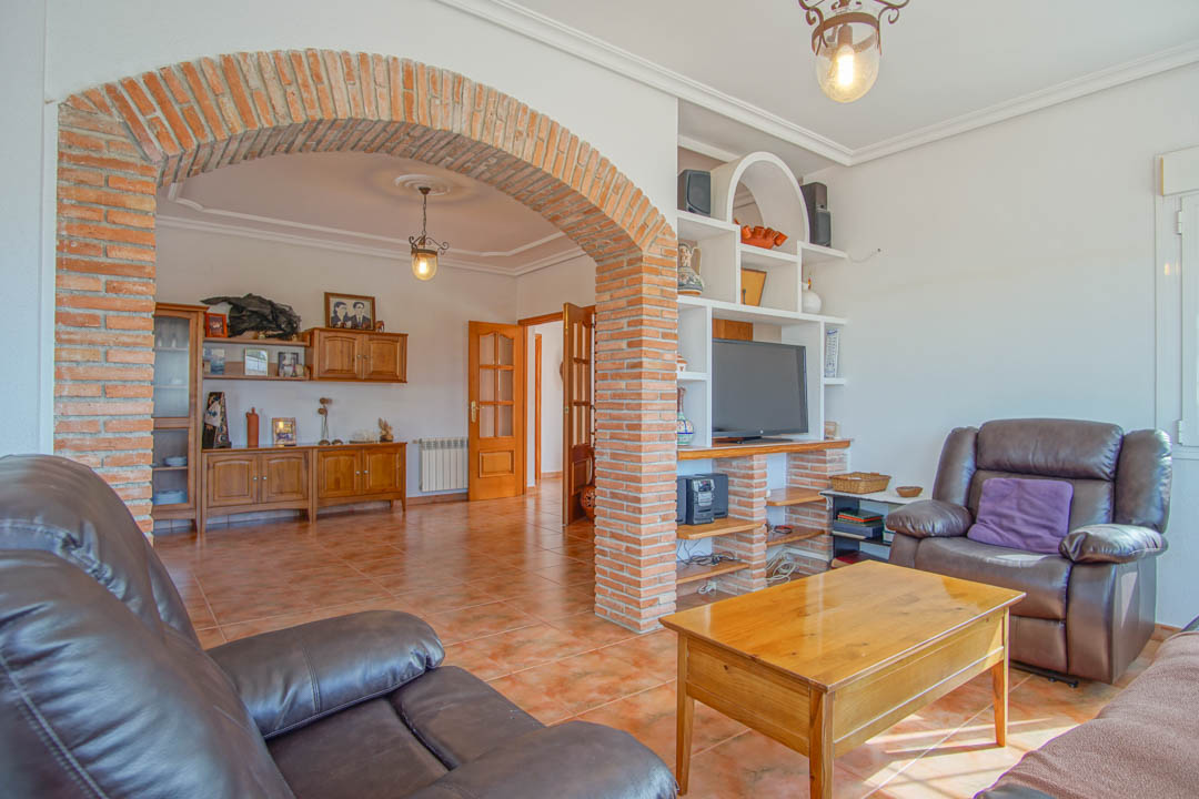 Living room featuring a prominent exposed brick archway, terracotta tile flooring, and solid wood furniture. Includes a built-in media shelving unit and natural light.