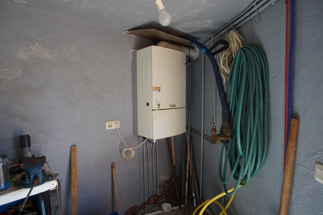 Practical storage room featuring a wall-mounted boiler, a workbench with a vise, and dedicated space for garden equipment and irrigation hoses.