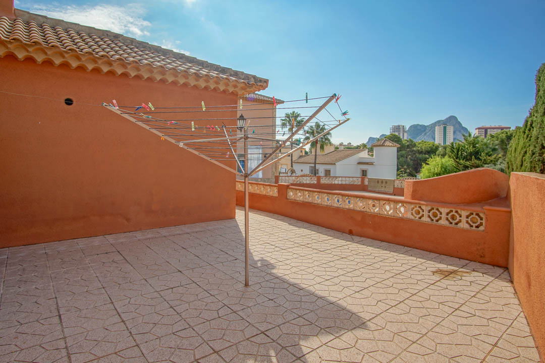 Solarium terrace featuring patterned floor tiles and terracotta walls, with distant views of the Peñón de Ifach and the surrounding neighborhood.