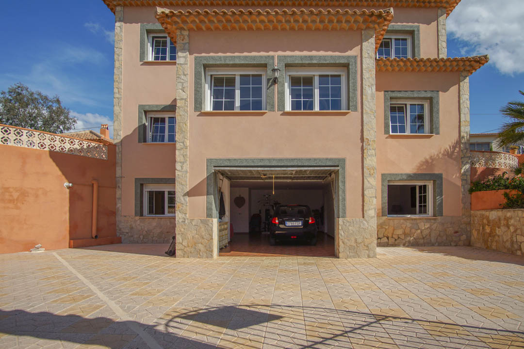 Three-story main facade featuring a spacious integrated garage, natural stone accents, and a large patterned tile driveway for multiple vehicles.