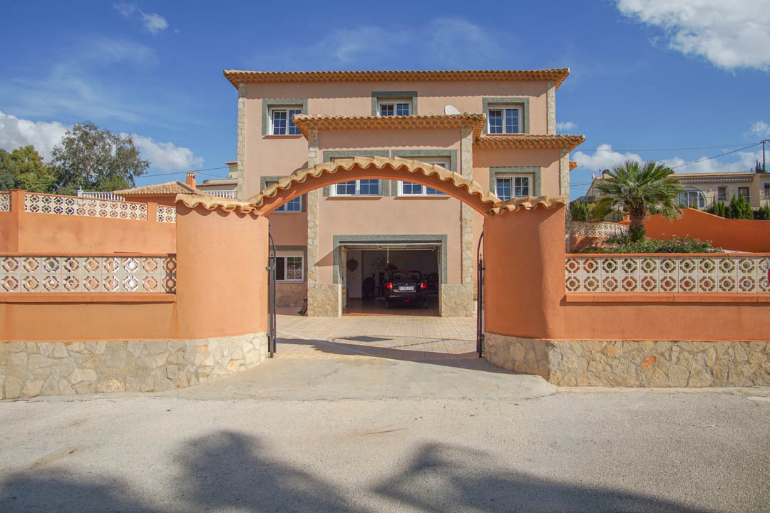 Three-story villa facade featuring a tiled arched entrance, terracotta perimeter walls with decorative lattice, and a ground-floor garage.