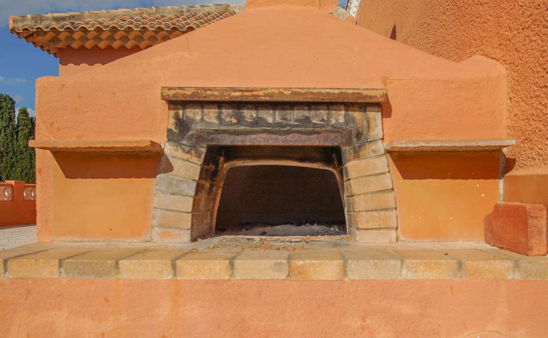 Traditional outdoor wood-fired oven built into a terracotta masonry structure with brick detailing and a classic tiled roof.