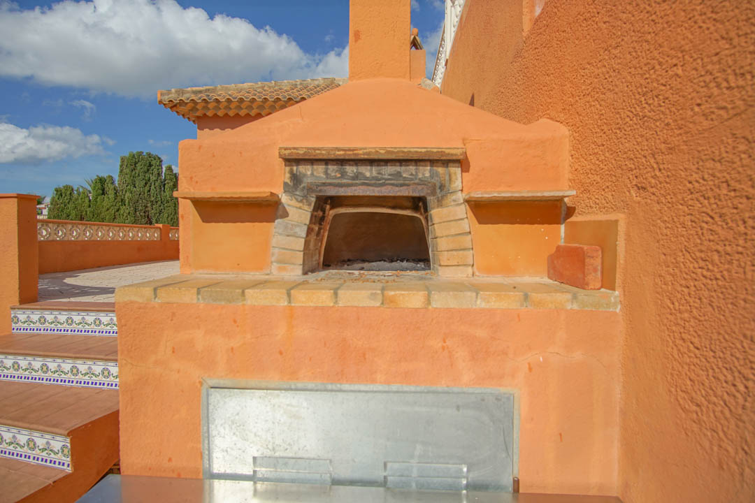 Traditional wood-burning oven integrated into the outdoor terrace, featuring a brick arch and chimney set against terracotta-toned walls.
