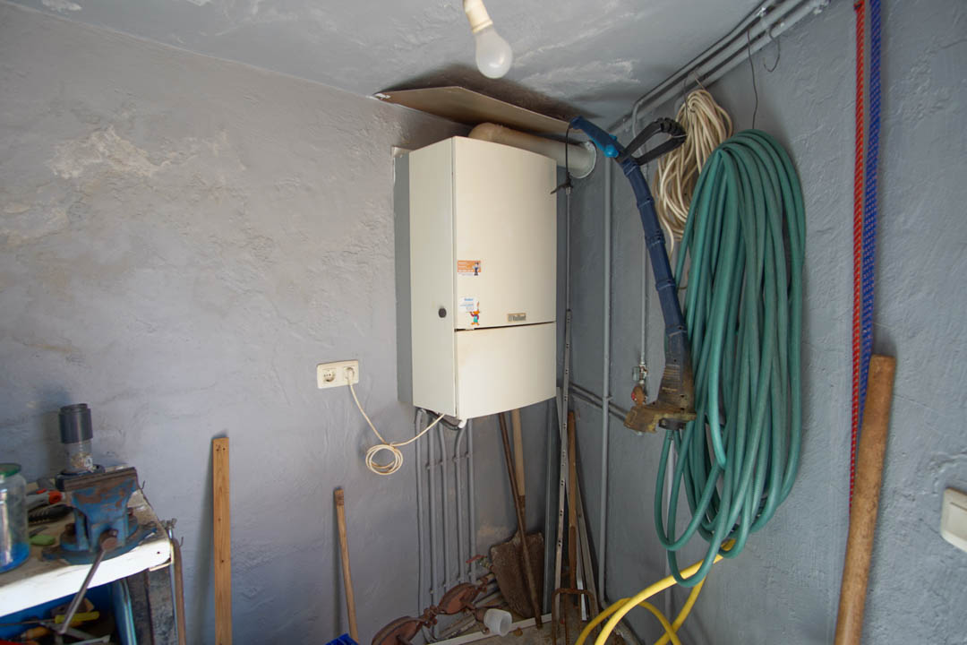 Utility and storage area featuring a wall-mounted boiler, a workbench with a metal vise, and dedicated space for garden tools and hoses.