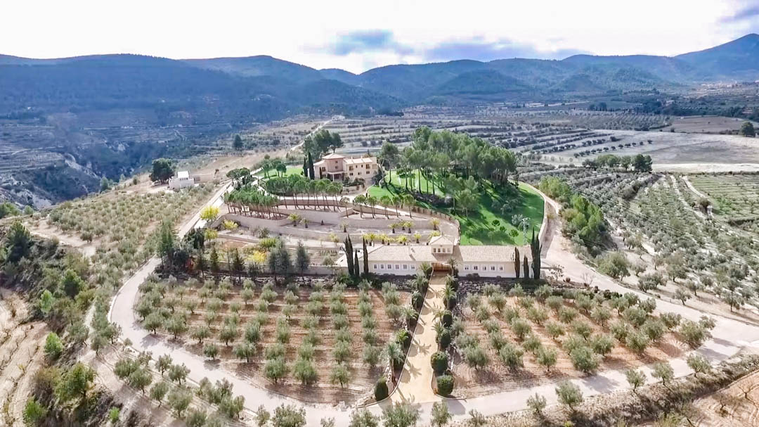 Aerial view of the estate featuring the main villa, the porter's house, and terraced olive groves set against a backdrop of scenic mountain valleys.
