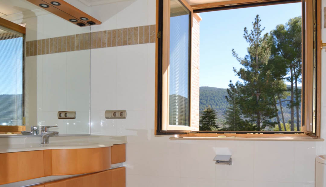 Bathroom featuring a wooden vanity, large mirror, and an open window framing scenic views of the surrounding pine forests and mountain range.