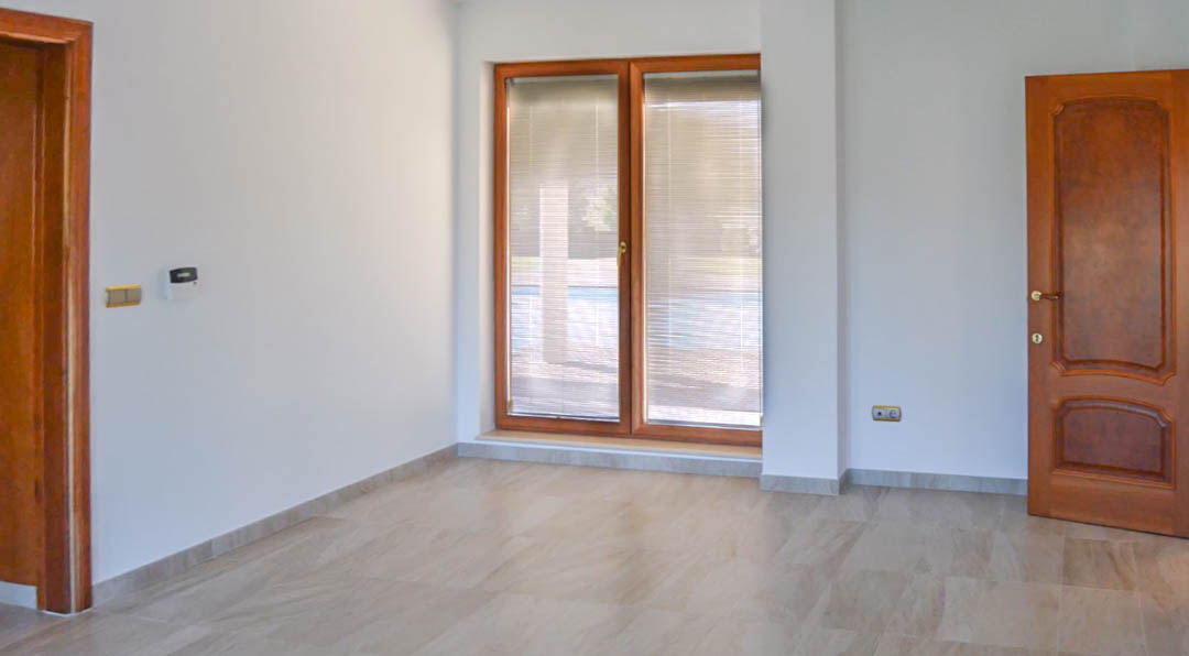 Bright room featuring natural stone flooring, high-quality solid wood doors, and large windows with integrated blinds overlooking the terrace area.