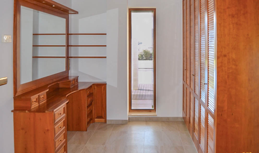 Dressing room featuring a high-quality wooden vanity, built-in wardrobes with louvered doors, and a vertical window for natural light.
