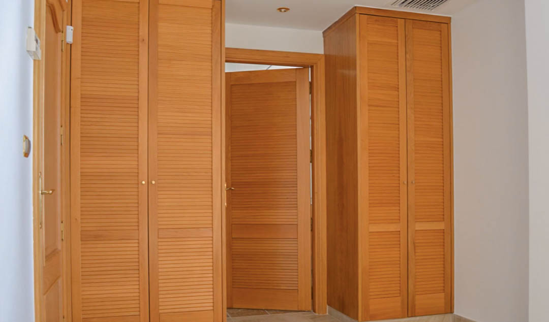 High-quality built-in wooden wardrobes with slatted doors, featuring matching interior woodwork and recessed ceiling lighting in a bright hallway.