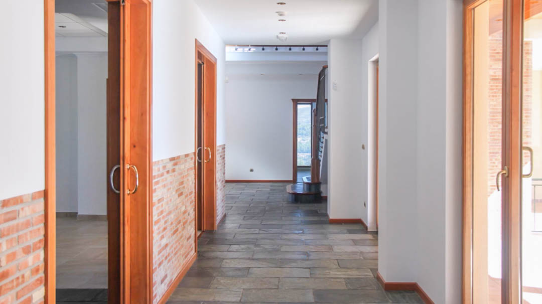 Interior hallway featuring natural stone flooring, exposed brick wainscoting, and solid wood door frames. The space includes recessed ceiling lighting and leads toward the staircase.