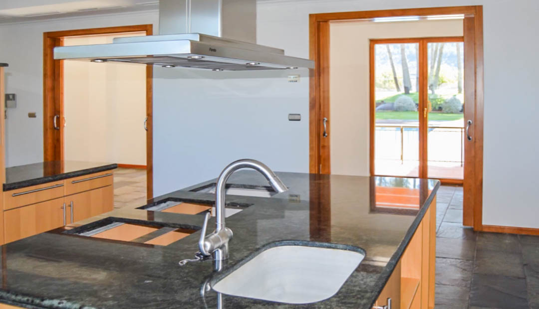 Kitchen featuring a dark granite island with integrated sink, stainless steel extractor, and stone flooring. Large wooden sliding doors provide garden views.