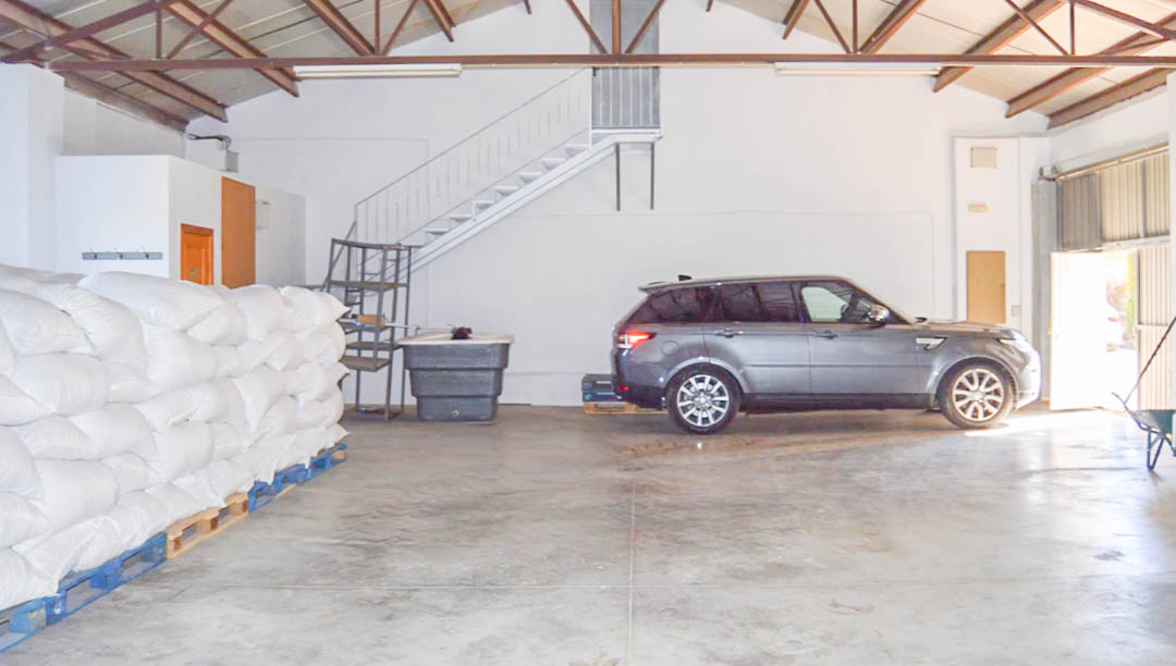 Spacious industrial warehouse featuring polished concrete floors, exposed metal roof trusses, and ample room for vehicles and agricultural storage on pallets.