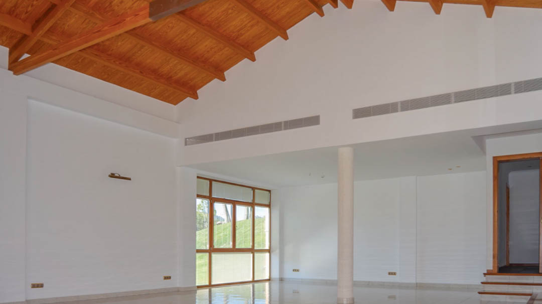 Spacious living room featuring a high vaulted ceiling with exposed wooden beams, polished tile flooring, and integrated linear air conditioning vents.