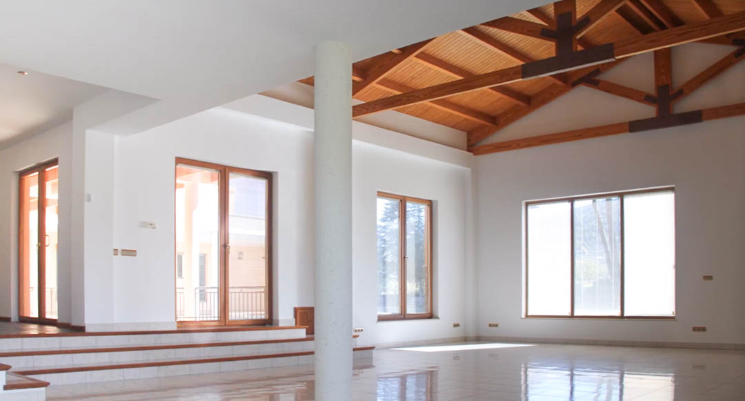 Spacious open-plan living area featuring high vaulted wooden ceilings with exposed beams, polished tile flooring, and large windows for natural light.