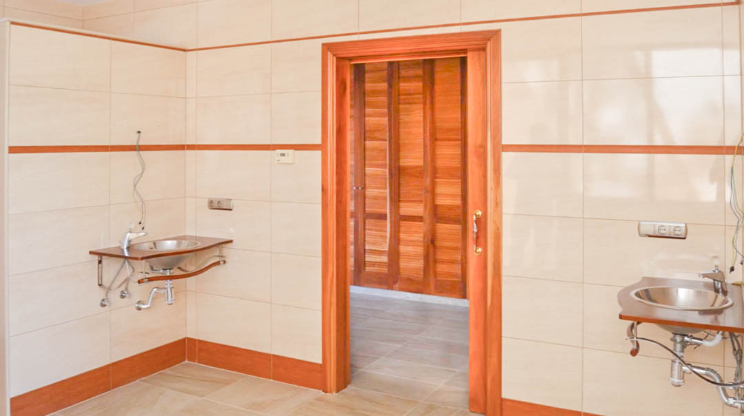 Utility or preparation room featuring tiled walls, twin stainless steel sinks on wooden supports, and a doorway leading to a wood-paneled interior space.