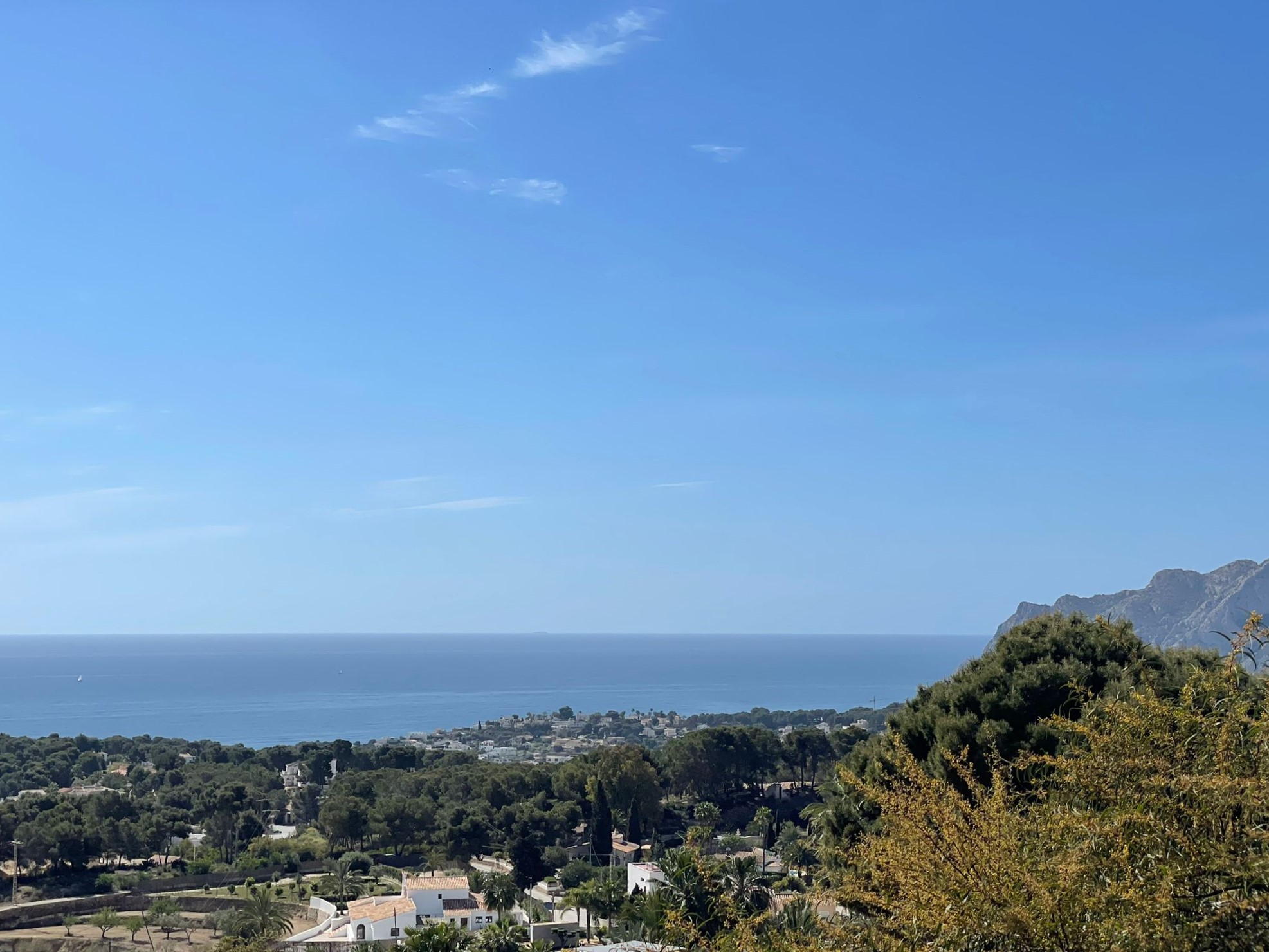 Panoramic view of the Benissa coastline, featuring Mediterranean vegetation, residential villas, and the sea under a clear blue sky.