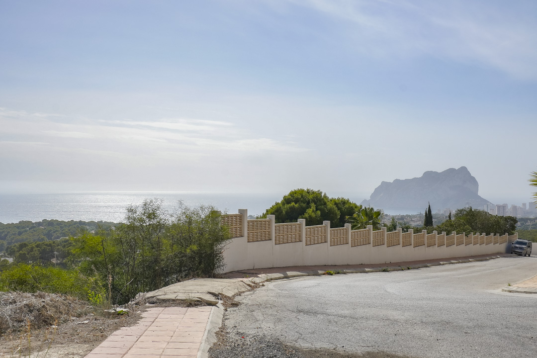 Street-level view overlooking the Mediterranean Sea and Peñón de Ifach, featuring a white perimeter wall with decorative lattice fencing and local greenery.