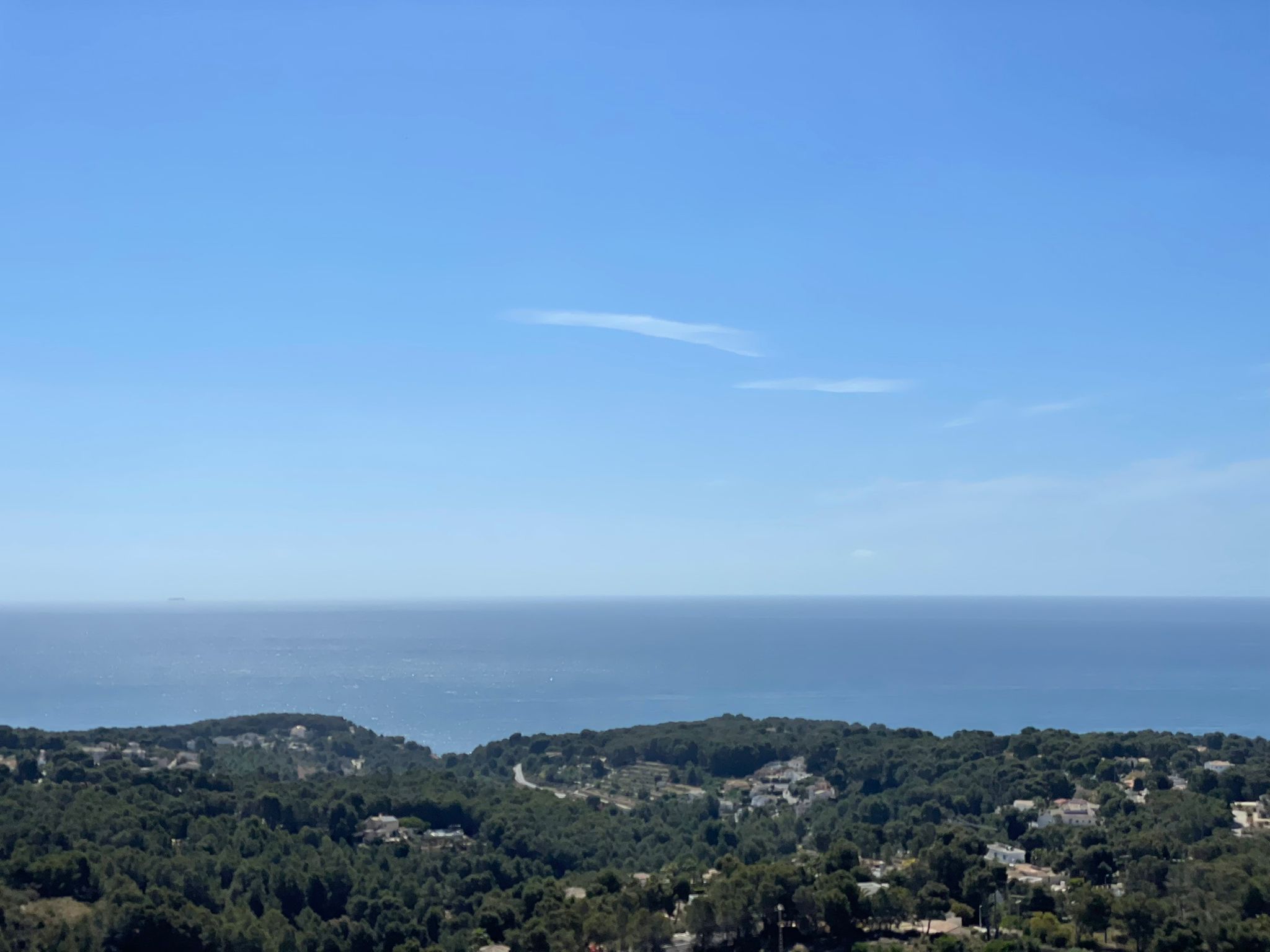 Elevated panoramic view overlooking the Mediterranean Sea and the lush pine-covered hills of Benissa under a clear blue sky.