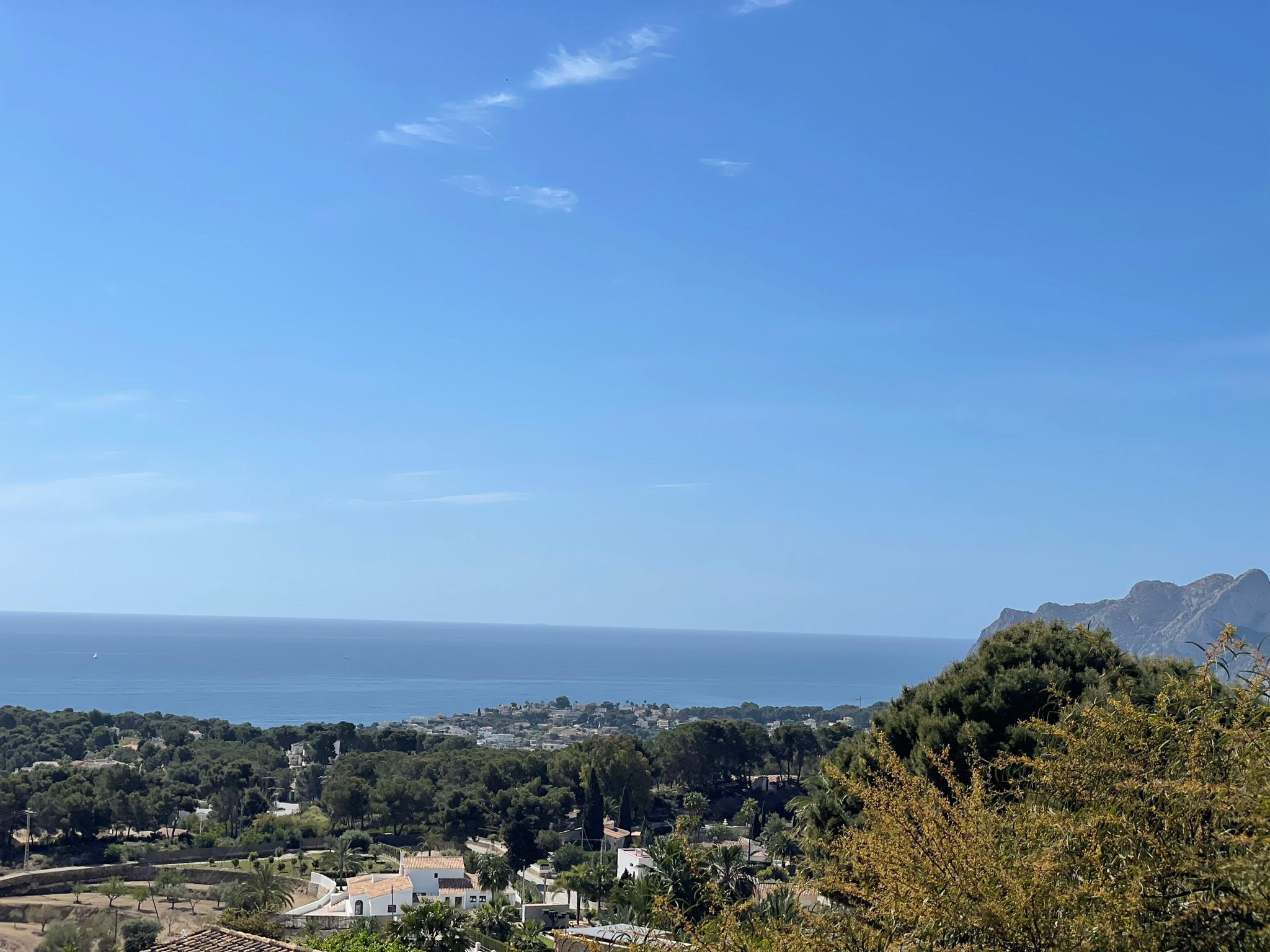 Panoramic view from the property overlooking the Benissa coastline, featuring lush Mediterranean greenery and the sea under a clear blue sky.